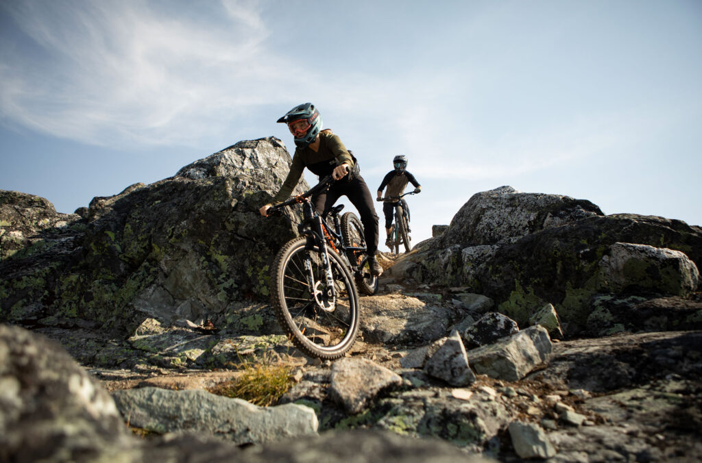 Two riders work their way around volcanic rock in the high alpine as they make their way down the trail.