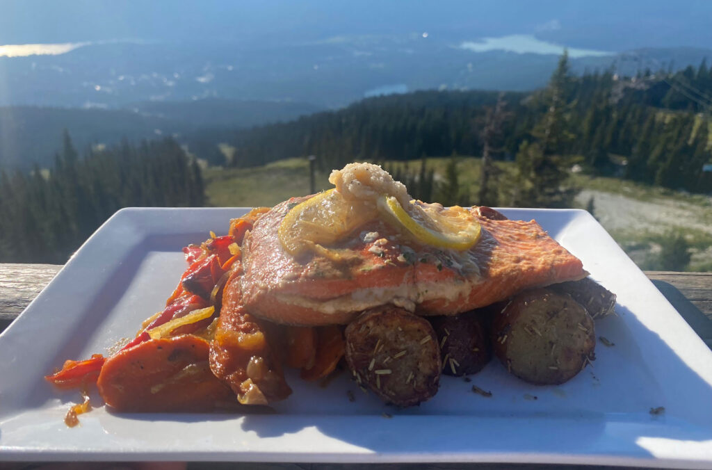 Cedar planked salmon served on rosemary potatoes and fresh vegetables, with a stunning view of the Coast Mountains as the backdrop.