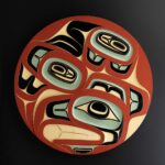 An Indigenous circular wooden carving coloured red, teal and black.