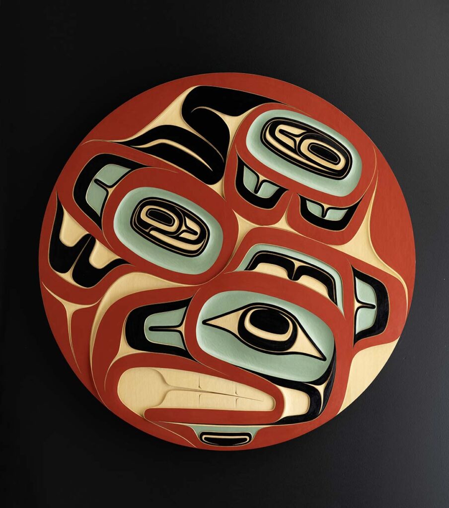 An Indigenous circular wooden carving coloured red, teal and black.