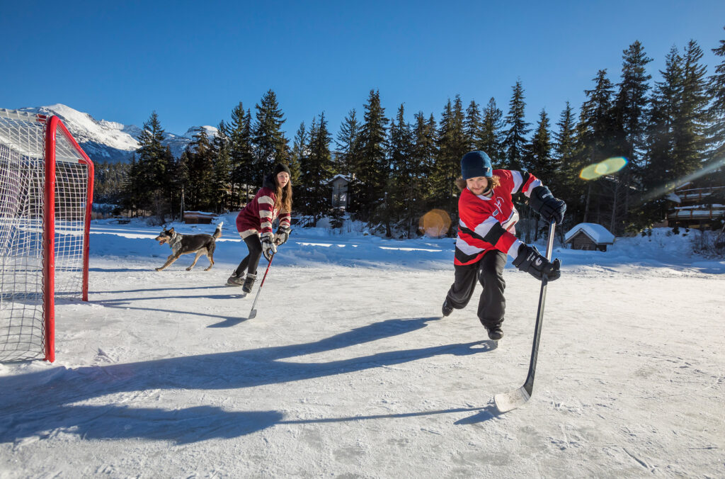 Two hockey players have fun on one of Whistler's frozen lakes in the winter sunshine.