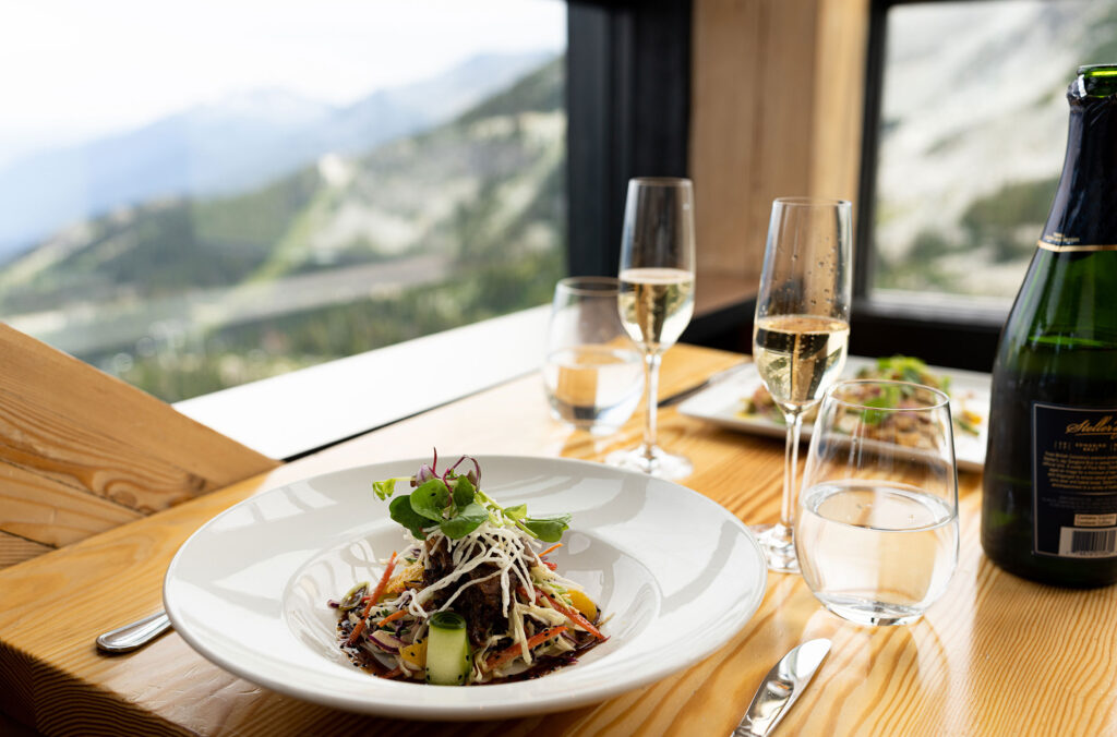 Colourful food and glasses of bubble set on a table overlooking the Coast Mountains at Christine's on Whistler Blackcomb