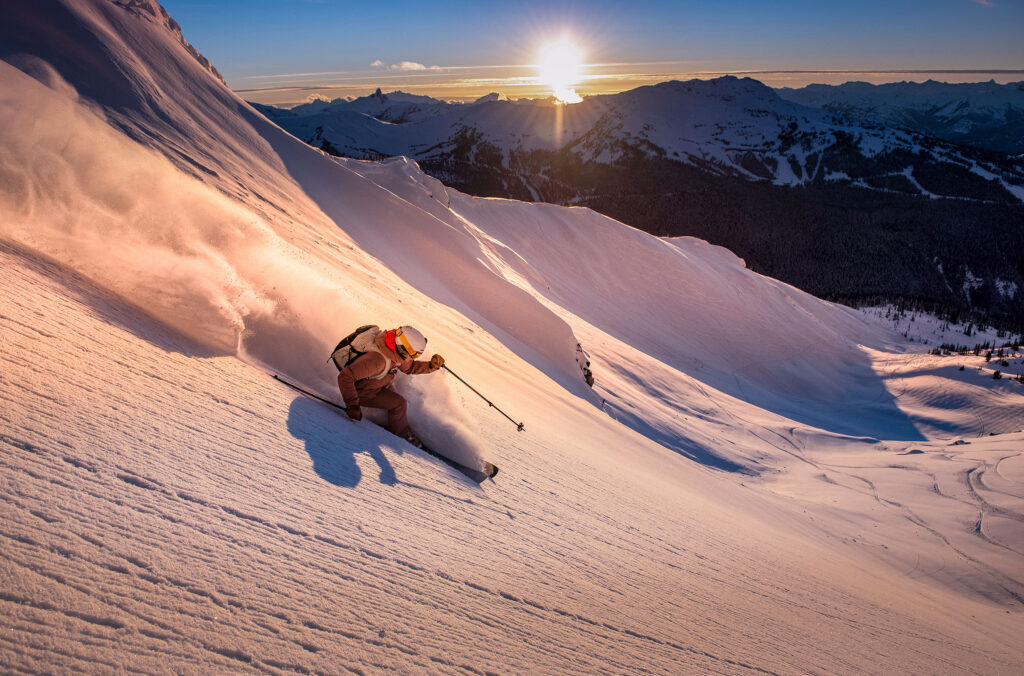 A skier enjoying fresh powder on the slopes of Whistler Blackcomb in the sun.