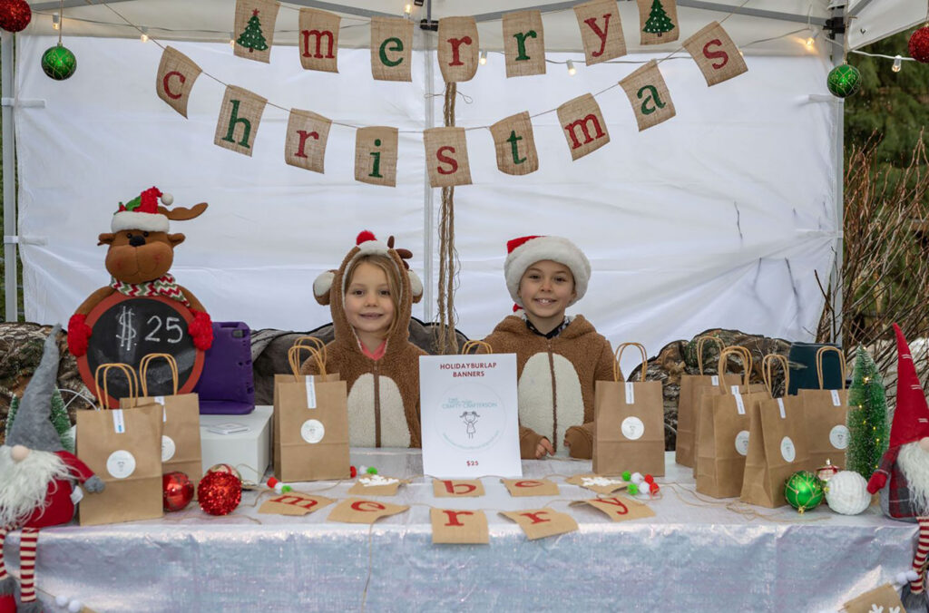 Two young entrepreneurs stand at their festive banner booth at Bratz Biz in Whistler.
