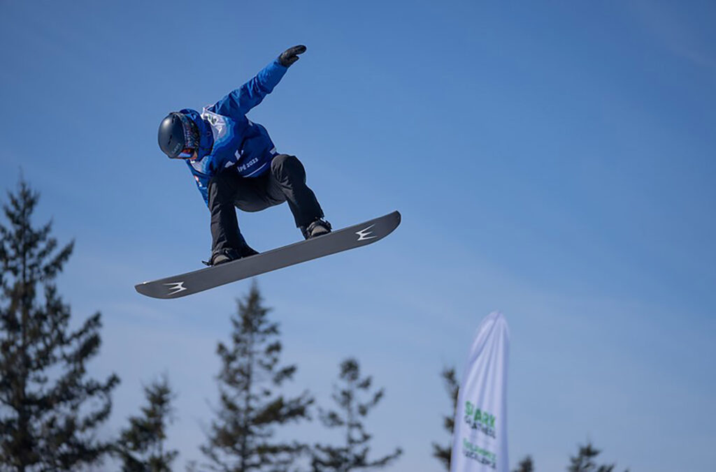 A photo of athlete Anthony Shelly in the air on his snowboard while competing at an event. 