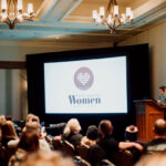 Ashlie stands at the front of the stage to start a 100 Women Who Care Whistler meeting.