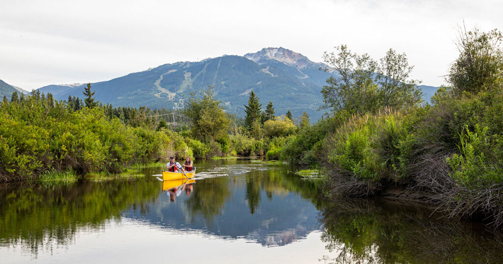 Two people navigate the River of Golden Dreams via canoe in the summer months in Whistler.