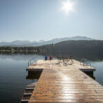 Two people sitting on a dock looking out to Alta Lake as the sun shines.