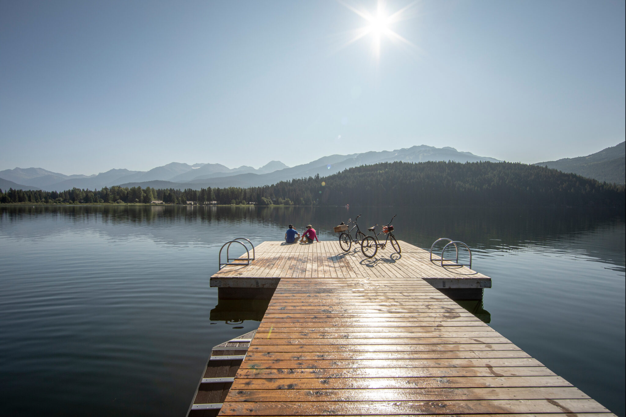 Two people sitting on a dock looking out to Alta Lake as the sun shines.