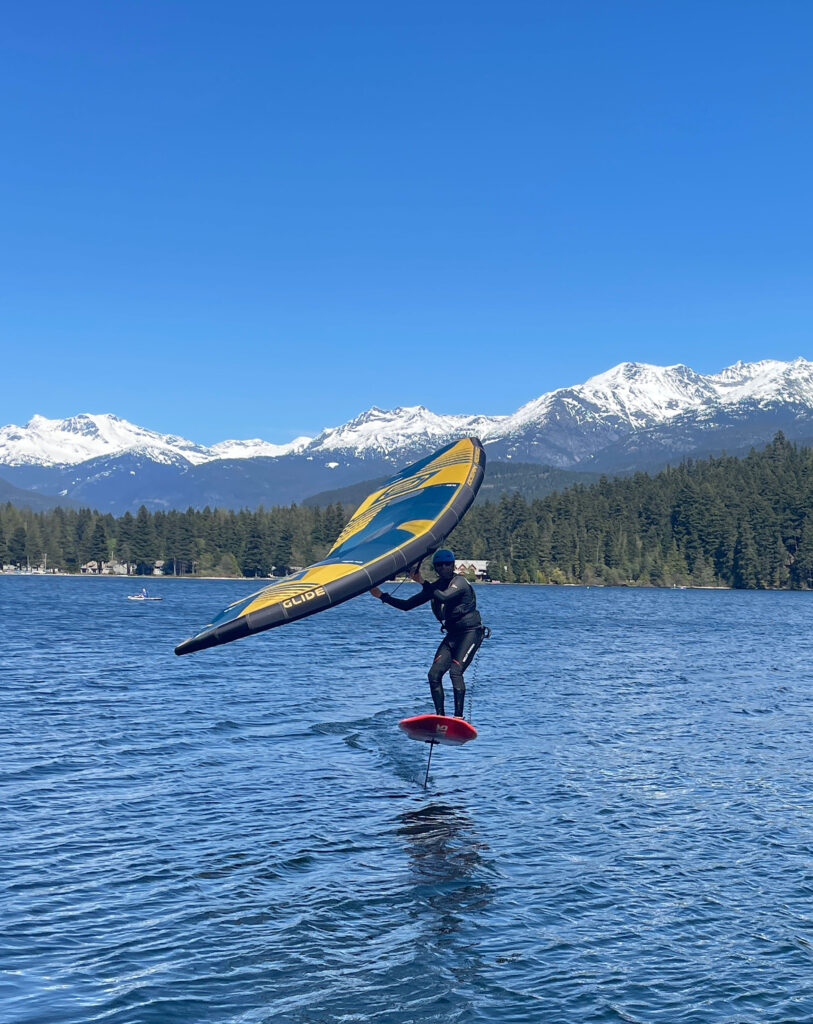 A person on a wing foil slices through the blue waters of Alta Lake in Whistler.