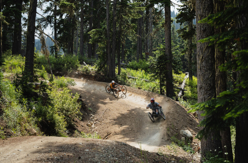 Two adaptive mountain bike riders make their way down the berms of the Whistler Mountain Bike Park.