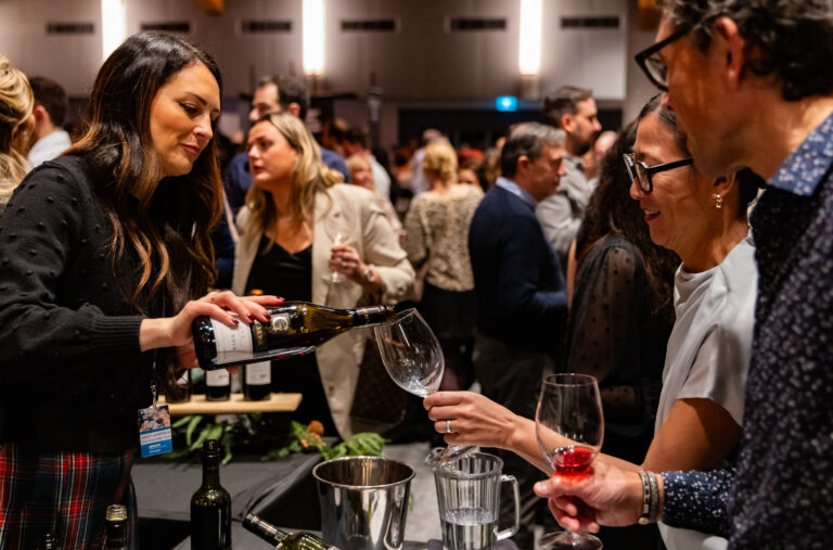 A person reaches across a table to have their wine glass filled at a Cornucopia event in Whistler.