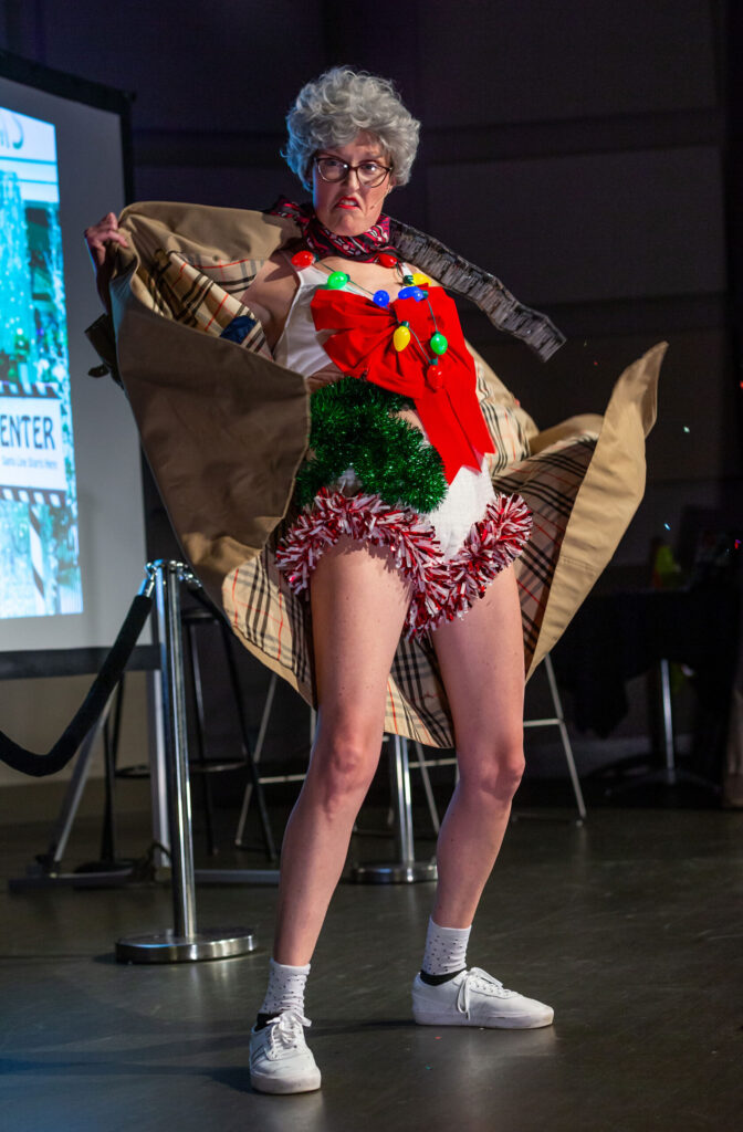 A comedic performer stands on the stage flaunting a funny, festive outfit. 