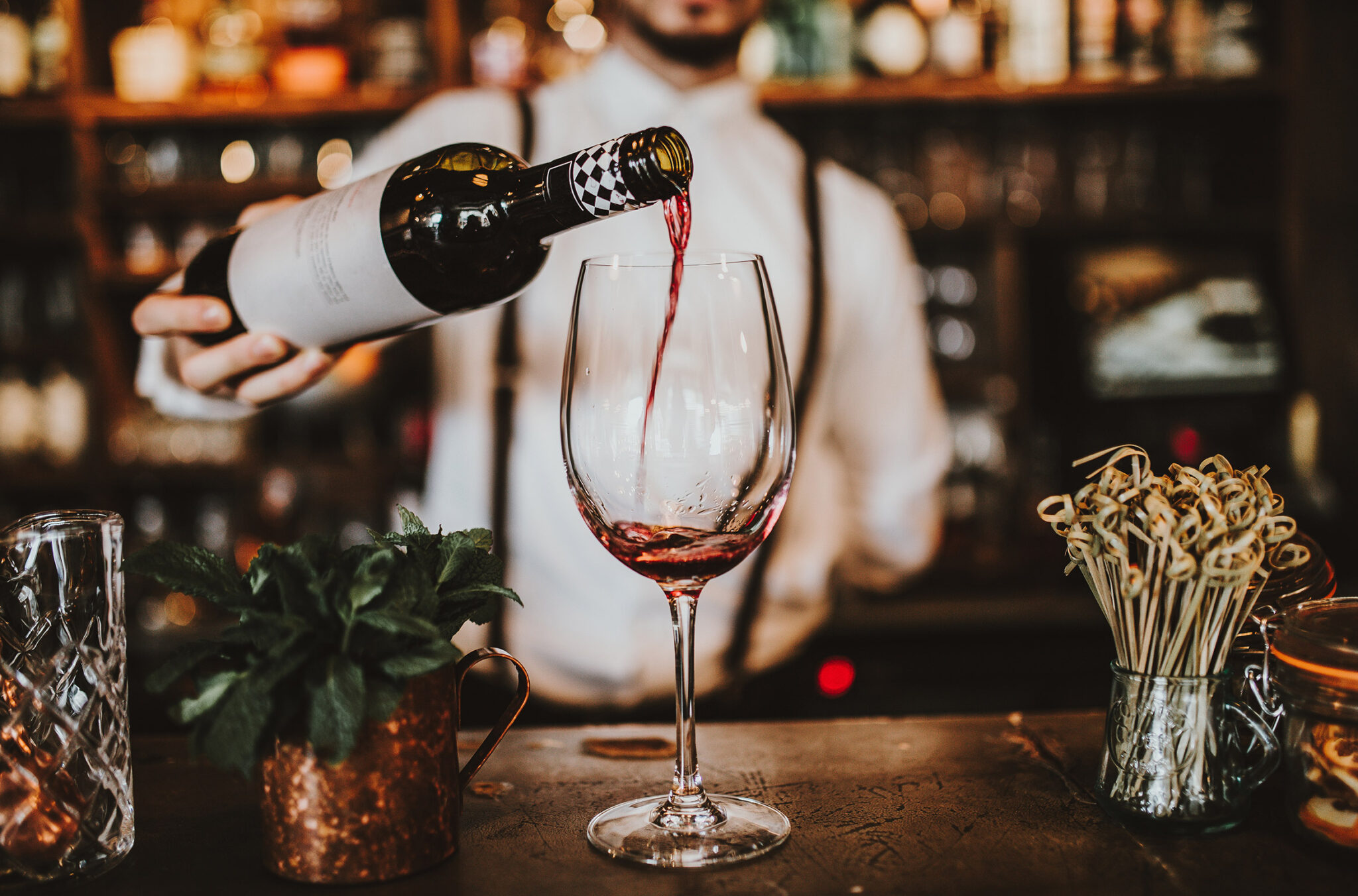 A server pours a glass of red wine, which is sat on a wooden bar.