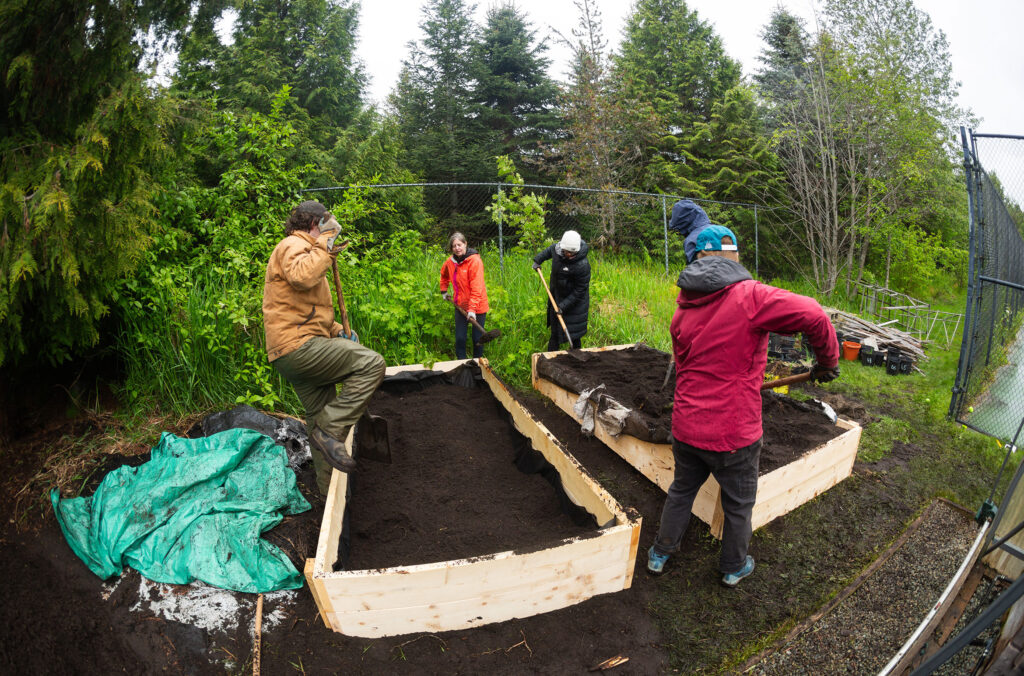 A group of people lay down dark soil in plant beds as part of AWARE's GROW program.