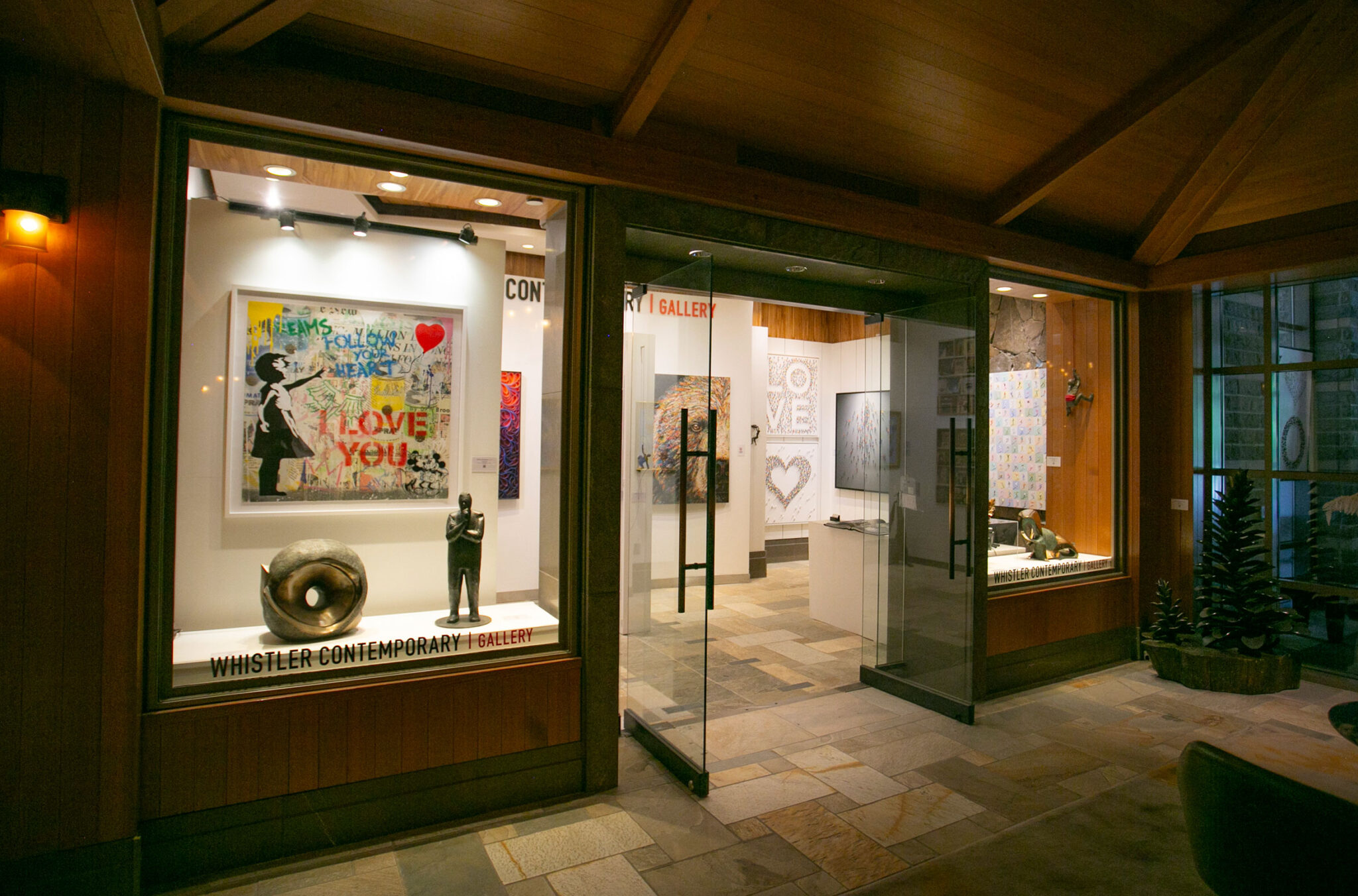 An outside shot of the Whistler Contemporary Gallery. It has glass windows and doors allowing you to see inside to a selection of colourful, modern art.