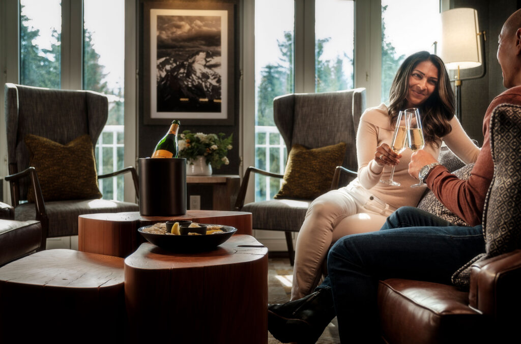 A couple sit on luxurious leather chairs drinking Champagne on the gold level of the Fairmont Chateau Whistler.