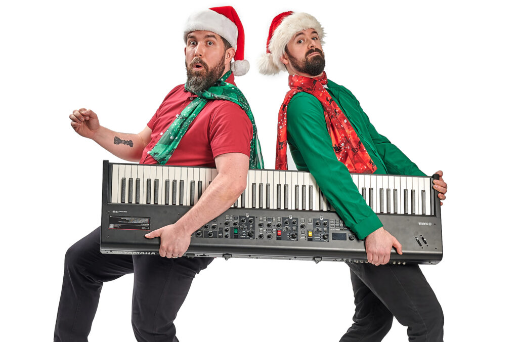 Two people hold a keyboard dressed in red, white and green, wearing Santa hats. 