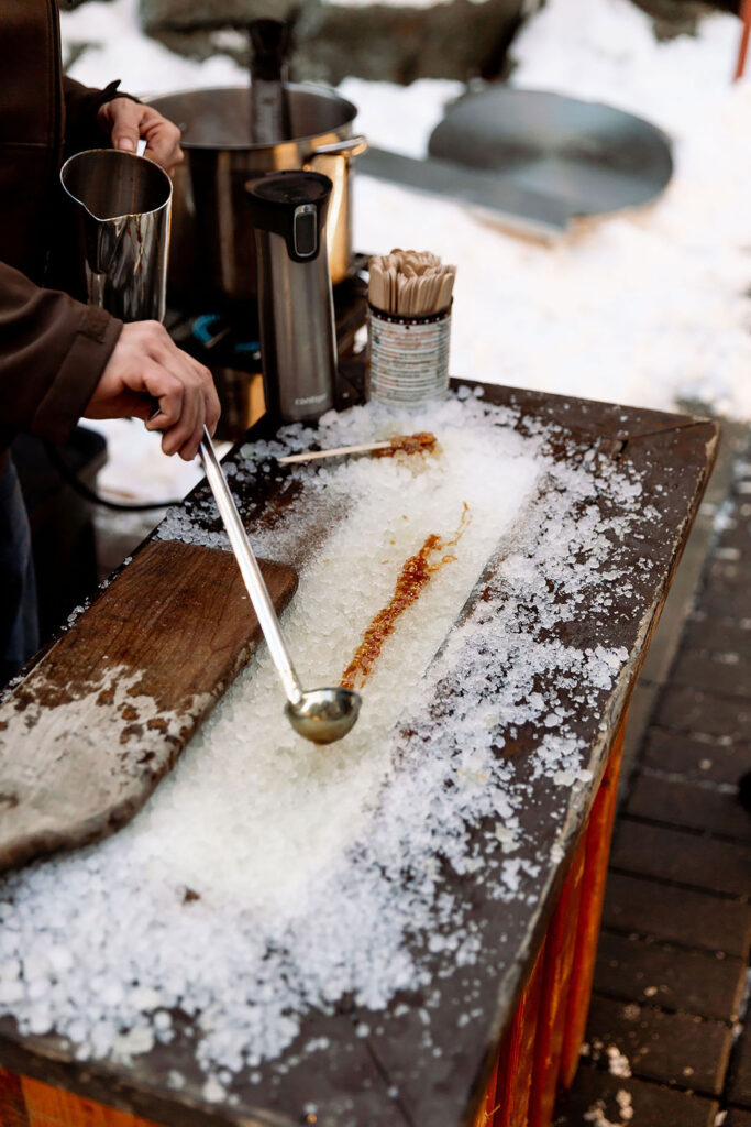 A person tries their hand at maple taffy making outside on the patio of the Four Seasons Whistler. They are using a ladle to spread syrup over ice.