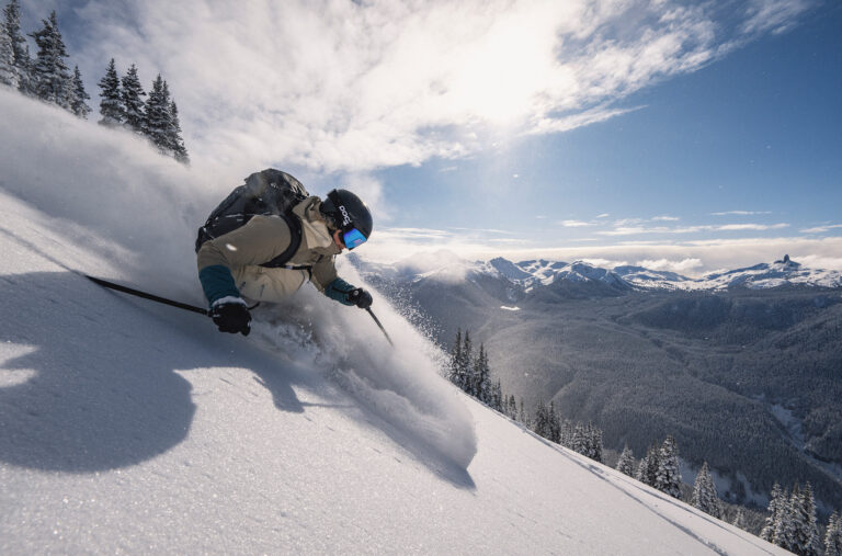 A skier heads down a slope of untouched snow on Whistler Blackcomb in the winter sunlight.