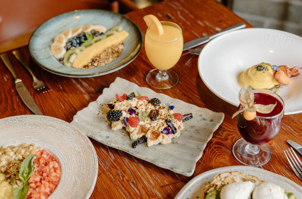 A table laid with a colourful selection of breakfast items like eggs bennies, waffles, fruit laden porridge and smoothies, served at the Braidwood Tavern at the Four Seasons Whistler.