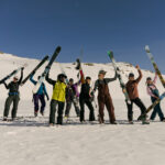 A group of people hold their skis up in the air cheering. They're on a women's camp with Extremely Canadian in Whistler's snowy backcountry.