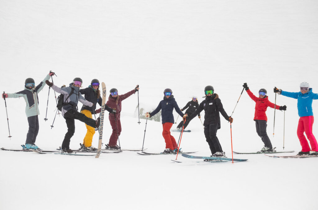 A group of skiers pose for the camera, raising their poles and skis like a cheer to celebrate a ski day on a women's camp in Whistler.