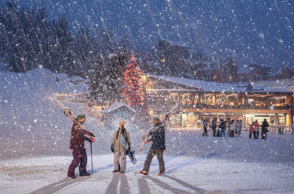 three people stand in the snow near whistler village gondola.