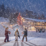 three people stand in the snow near whistler village gondola.