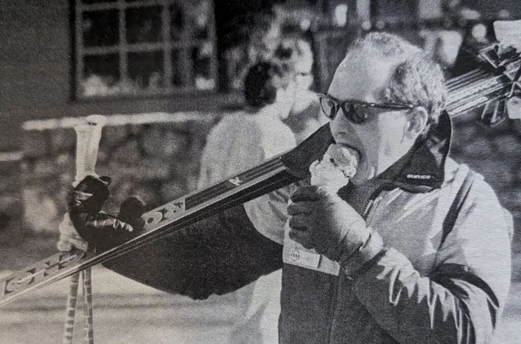 A retro black and white photo of a skier with skies over one shoulder enjoying an ice cream.