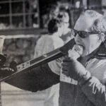 A retro black and white photo of a skier with skies over one shoulder enjoying an ice cream.