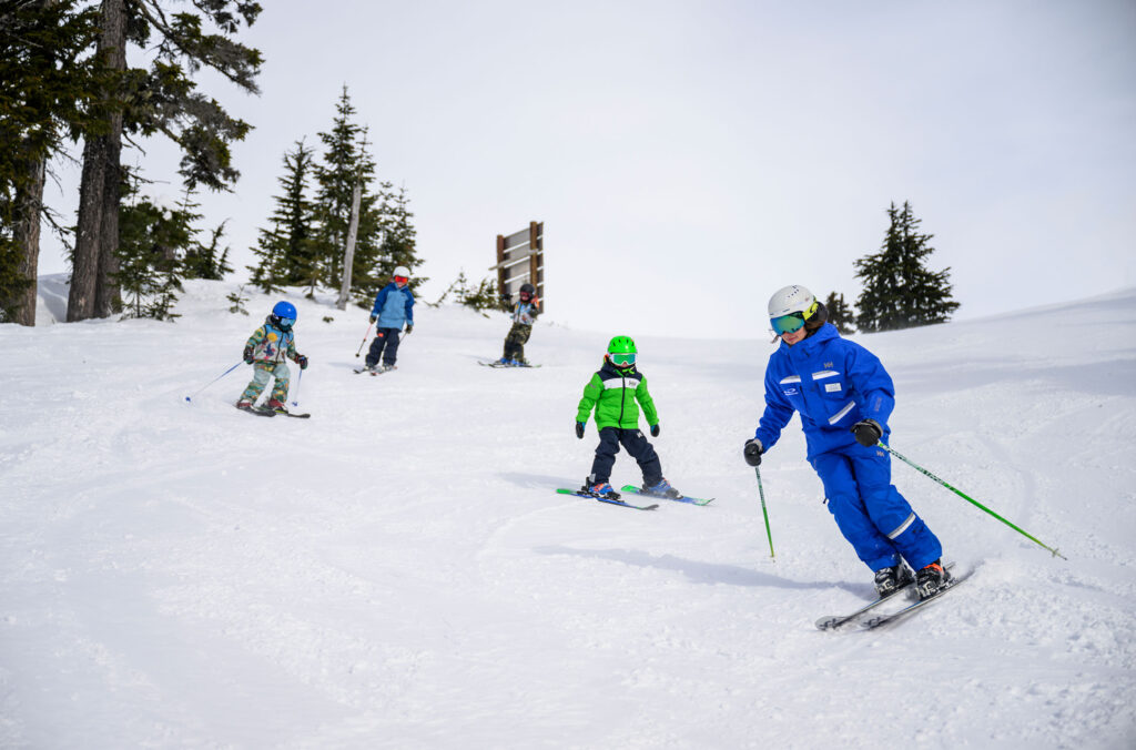 A ski instructor snakes down a ski slope on Whistler Blackcomb with four kids following.