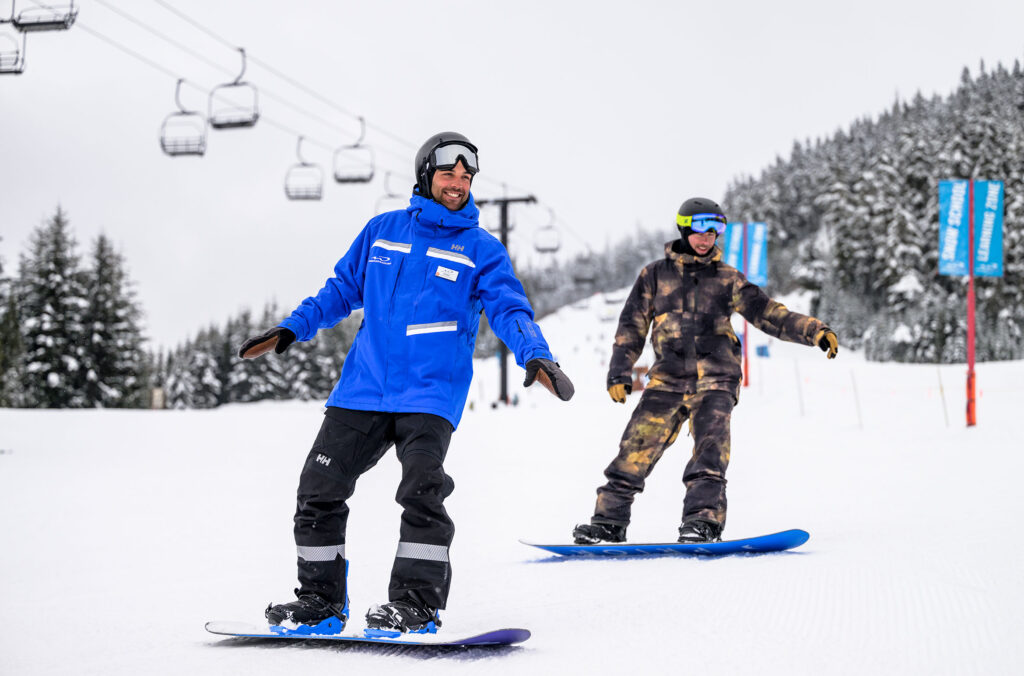 A snowboard instructor teaches an adult how to snowboard on Whistler Blackcomb.