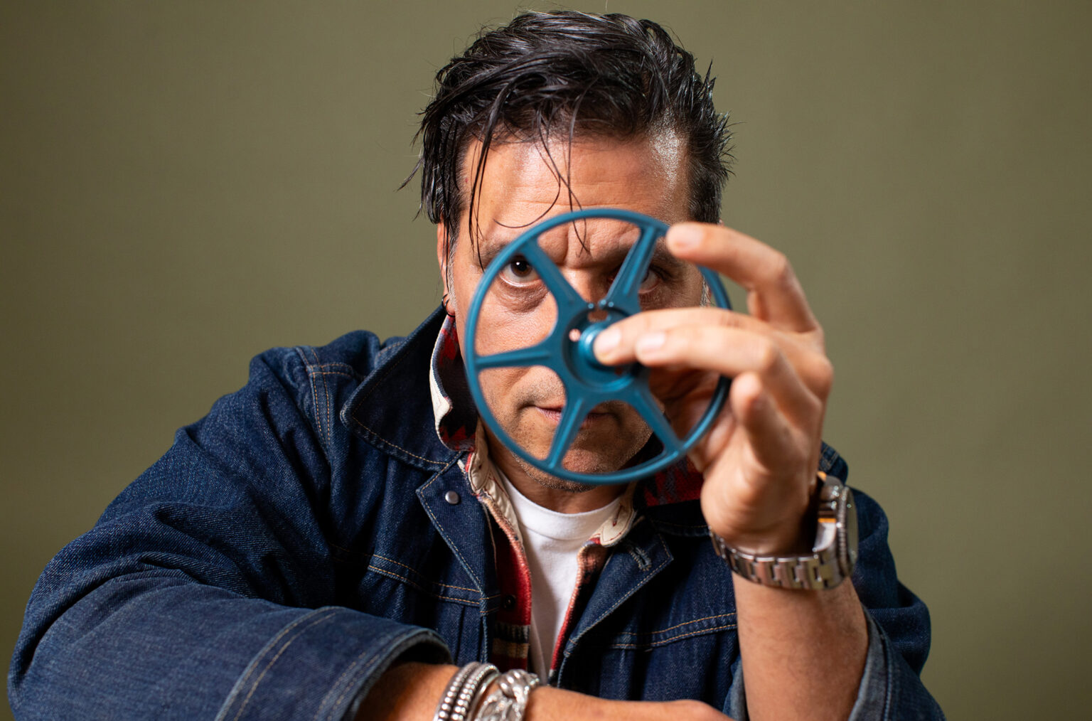 George Stroumboulopoulos holds an empty film reel in front of his face.