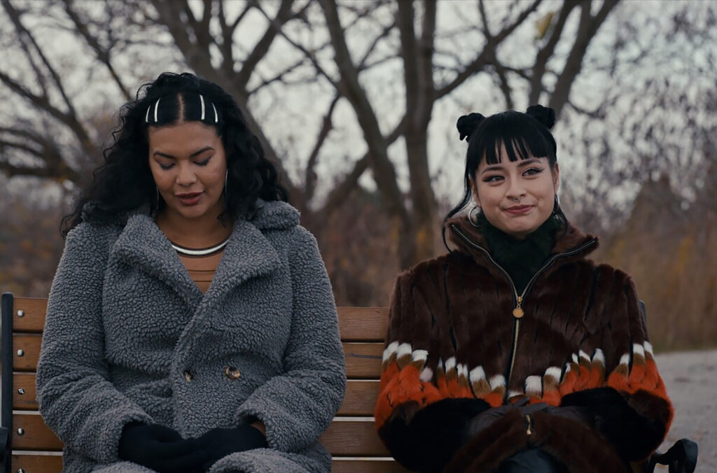 Two people sit on a park bench in winter wear. A shot from the move Nika & Madison.