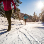 Two people cross-country ski in the sunshine at Whistler Olympic Park.