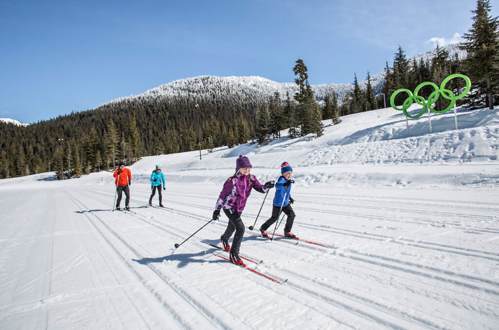 A family of four cross-country skis past the Olympic rings at Whistler Olympic Park.