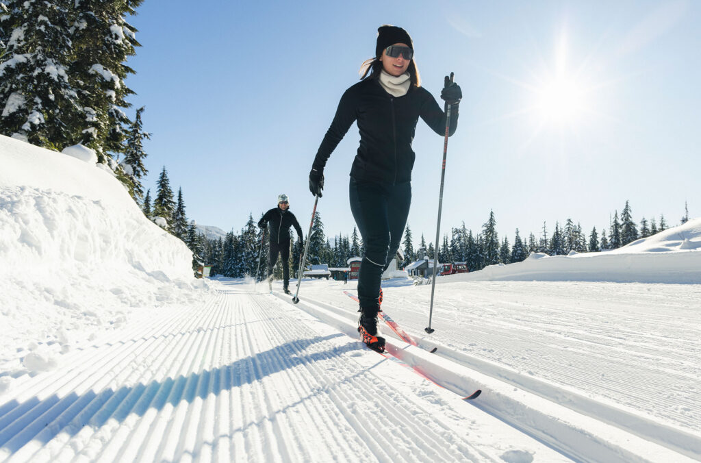 Two cross-country skiers glide on the beautifully groomed trails at The Callaghan in the sunshine.