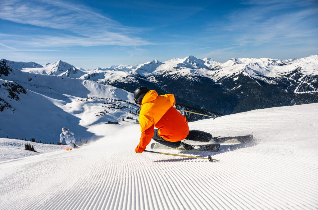 Two skiers charge down freshly groomed slopes on Whistler Blackcomb in the sunshine.