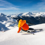 Two skiers charge down freshly groomed slopes on Whistler Blackcomb in the sunshine.