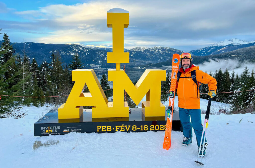 Combat diver, Alin Mirea stands in front of the I AM Invcitus Games sign on Whistler Mountain in his ski gear.