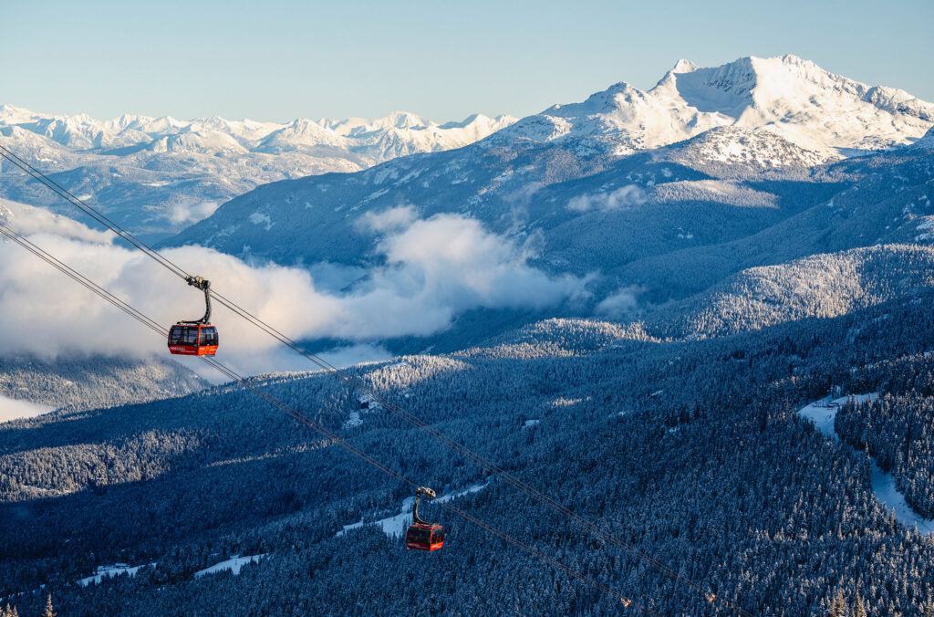 The PEAK 2 PEAK Gondola's red cabins soar above the valley between Whistler and Blackcomb mountains on a sunny, winter day.