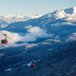 The PEAK 2 PEAK Gondola's red cabins soar above the valley between Whistler and Blackcomb mountains on a sunny, winter day.