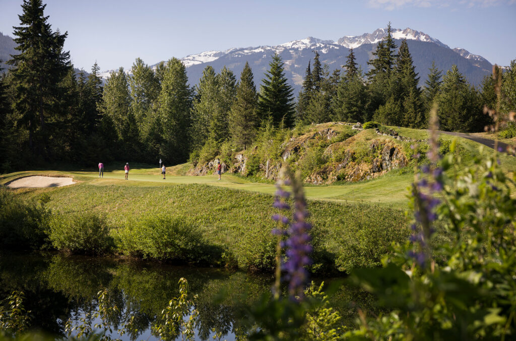 Golfers play on the lush greens of the Fairmont Chateau Whistler Golf Club with mountain views and beautiful wild flowers.