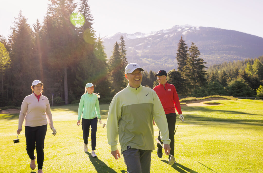 A group of golfers walk across the greens with the mountains in the background in Whistler.