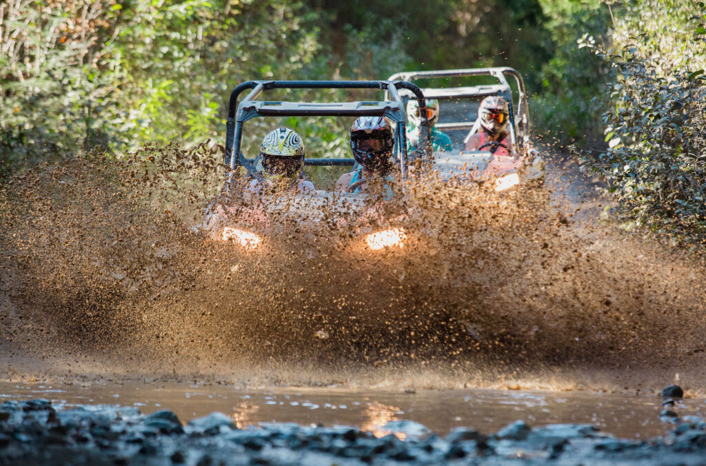 Two ATVs splash through a huge muddy puddle on a tour in Whistler.