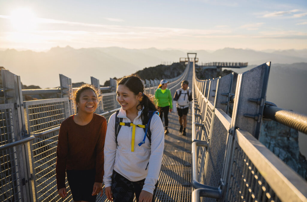 A family has fun crossing the Cloudraker Skybridge on Whistler Mountain in the summer sun.