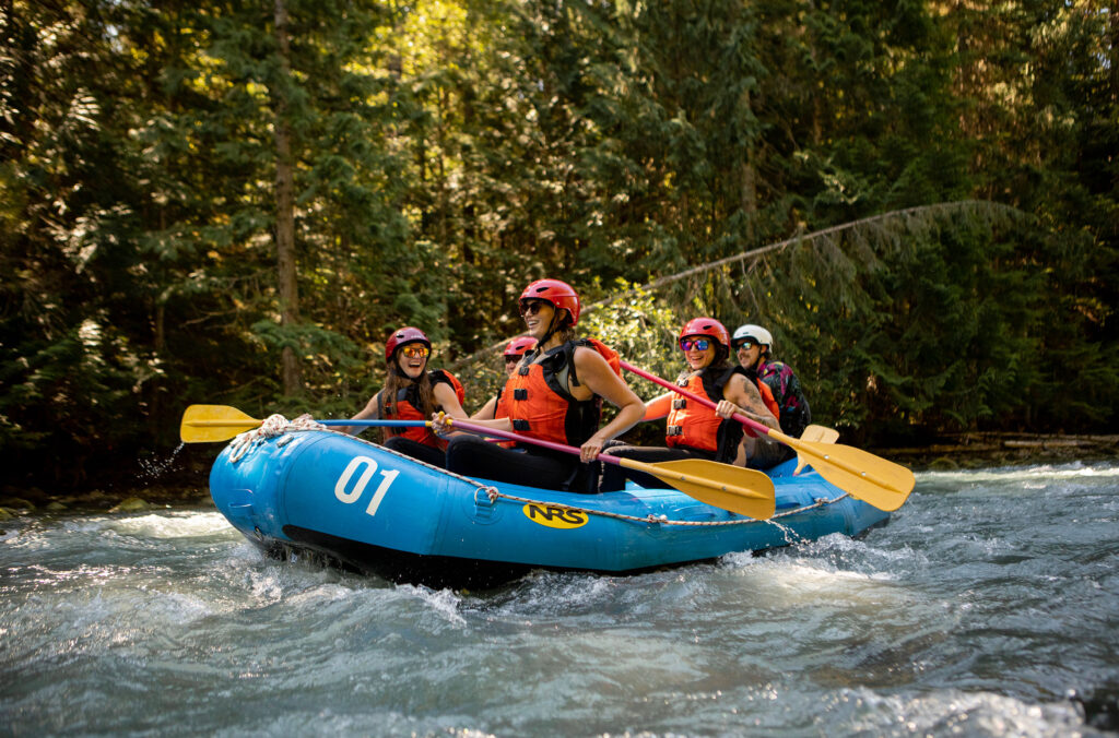 A group of people paddle in a whitewater raft on a river in Whistler.