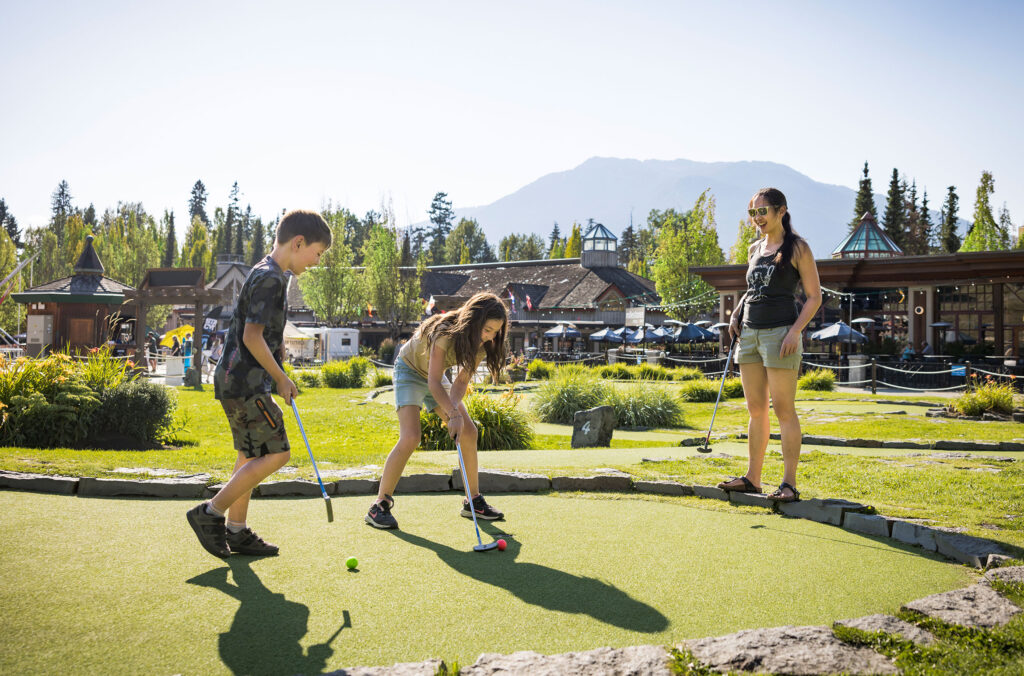 A family play mini golf at the base of Blackcomb in the summer sun.