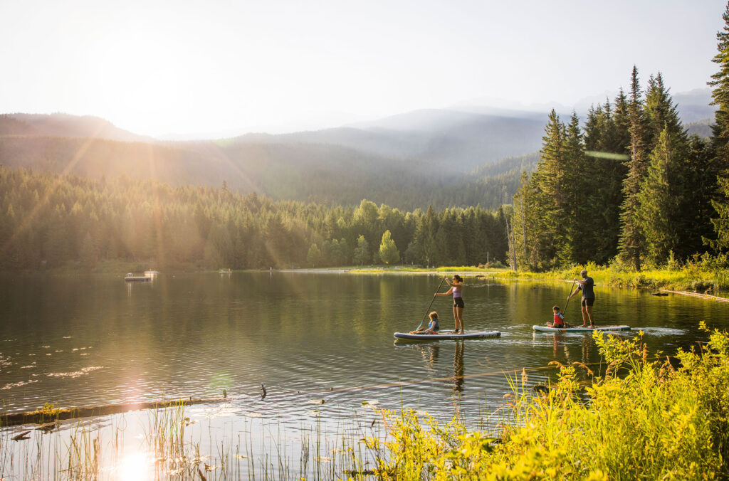 A family stand up paddle boards across Lost Lake in the summer sun.